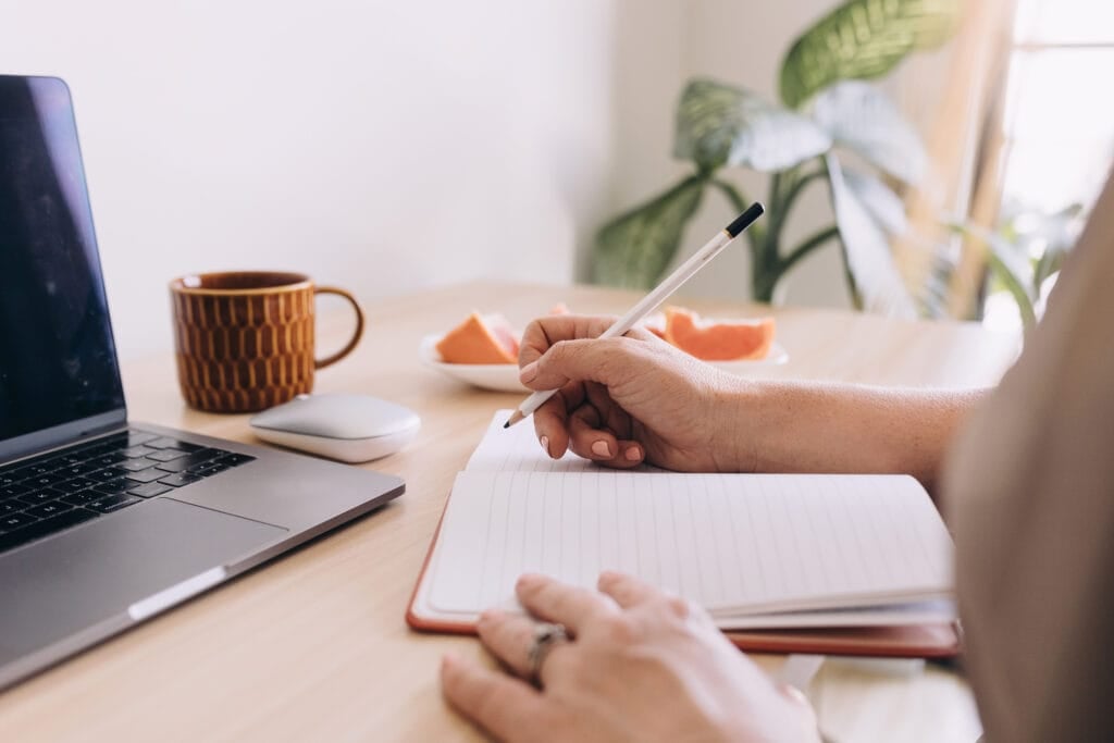 person writing in notepad at desk with laptop. How to make 10 dollars a day online