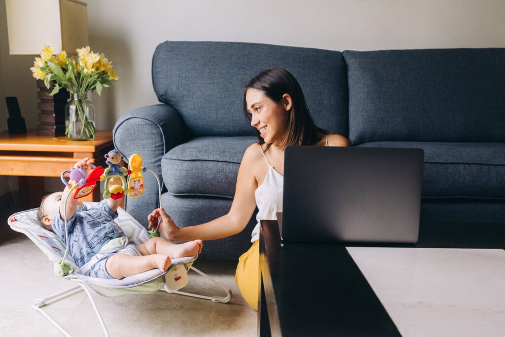 mom on laptop with baby playing in bouncer - Sell used baby items for cash